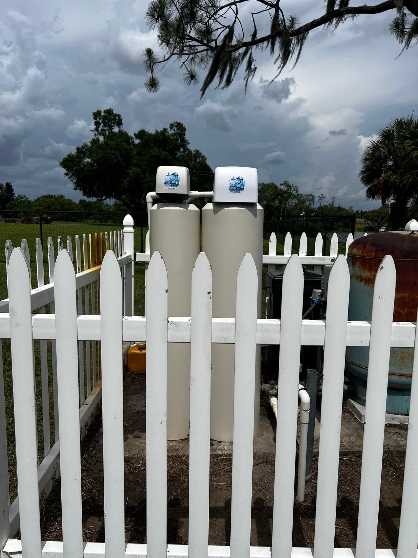Exterior dual-tank water softener and filtration system installed behind a white fence